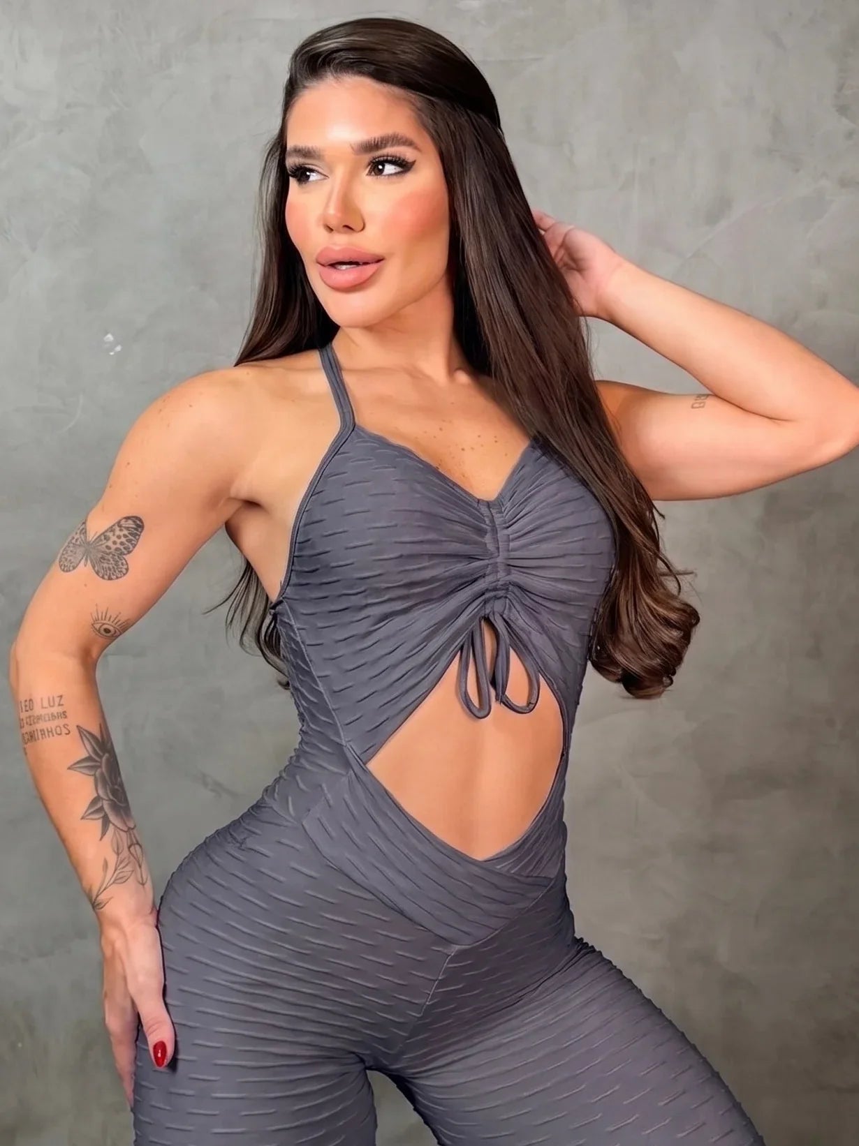 Woman wearing a gray jumpsuit with cut-out design against a gray background