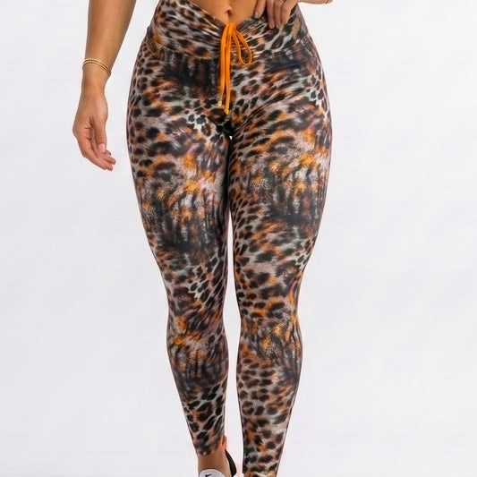 A woman modeling a matching activewear set consisting of a bright orange sports bra and high-waisted leopard-print leggings with an orange drawstring, paired with white sneakers, against a plain white studio background.