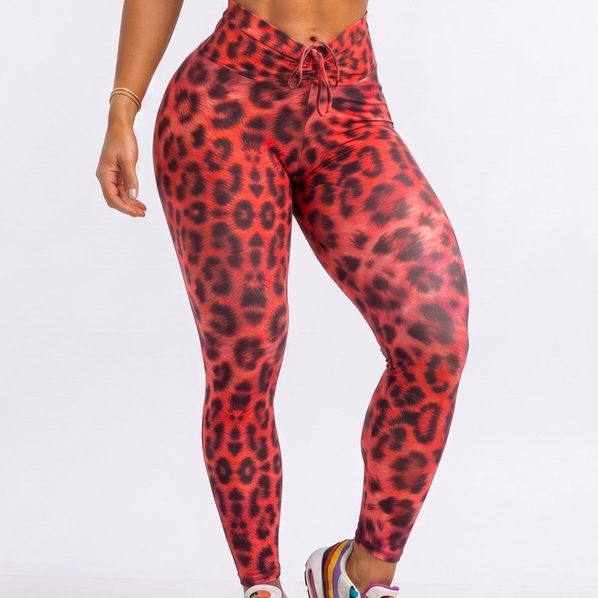 A woman modeling a matching red and black leopard-print activewear set, featuring a sports bra and high-waisted leggings, against a plain white studio background.
